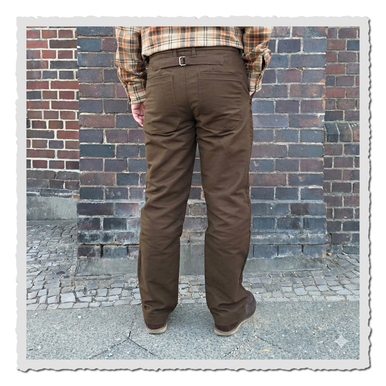 Rückansicht der Retronia Rudolph II Hose in Braun mit Cinch-Back, aufgesetzten Gesäßtaschen und geradem Bein vor Ziegelmauer.